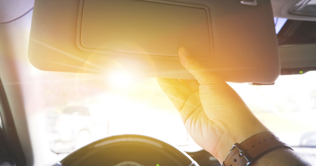 Man pulling visor down to block sun while driving