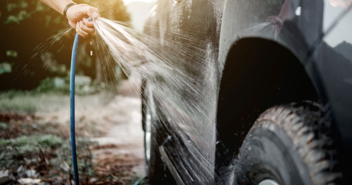 Man hosing down his jeep while washing it