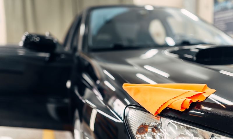 rag-on-the-hood-of-clean-car-on-carwash-service-BUHZQK9