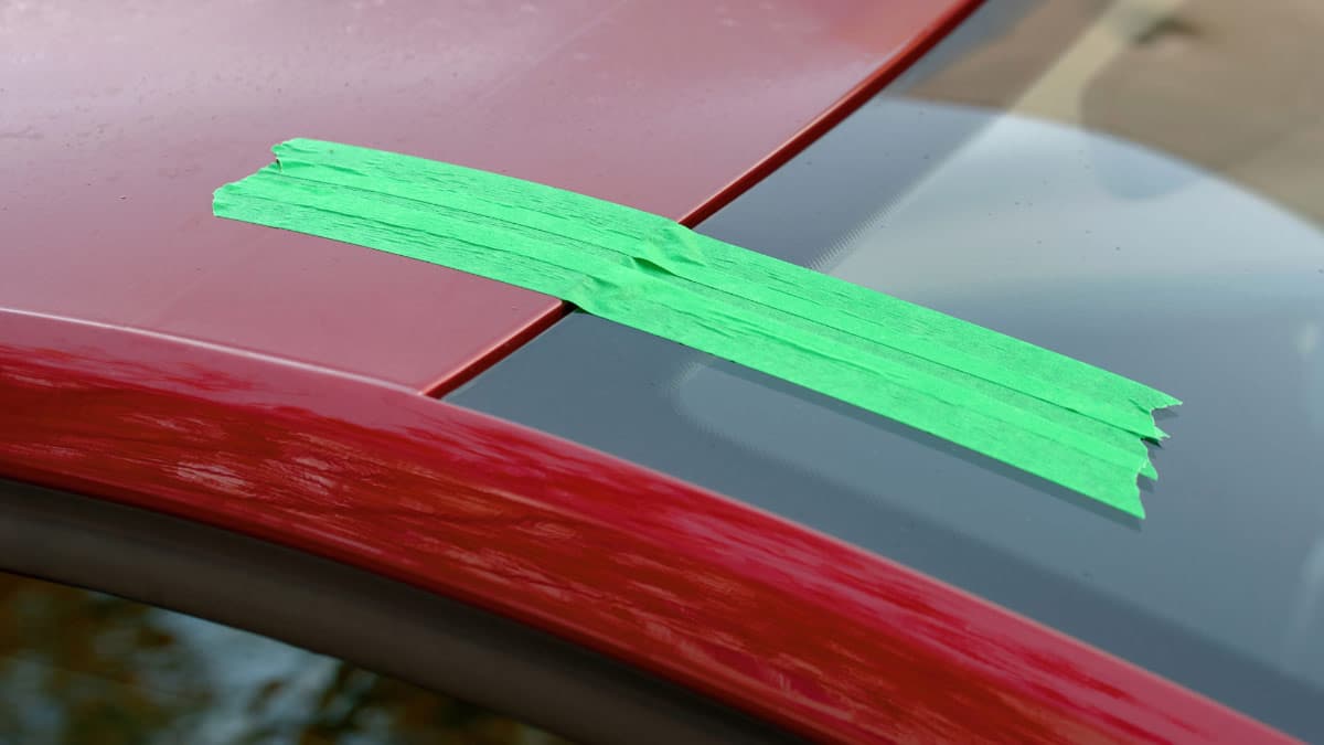 Red car with green masking tape holding new windshield in place after replacement