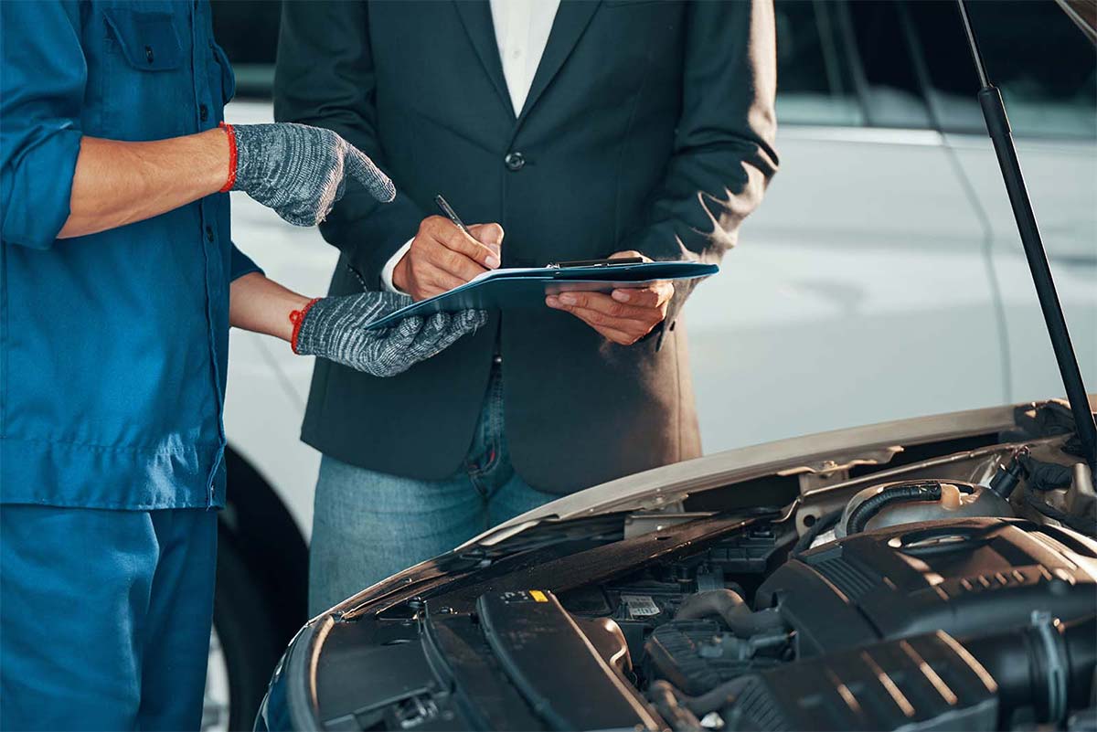 Mechanic and Car Owner Looking Under Hood Signing Paperwork