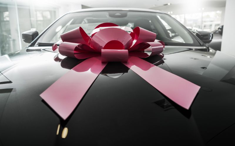 A picture of a brand new and shiny looking black car with a red holiday bow on it.