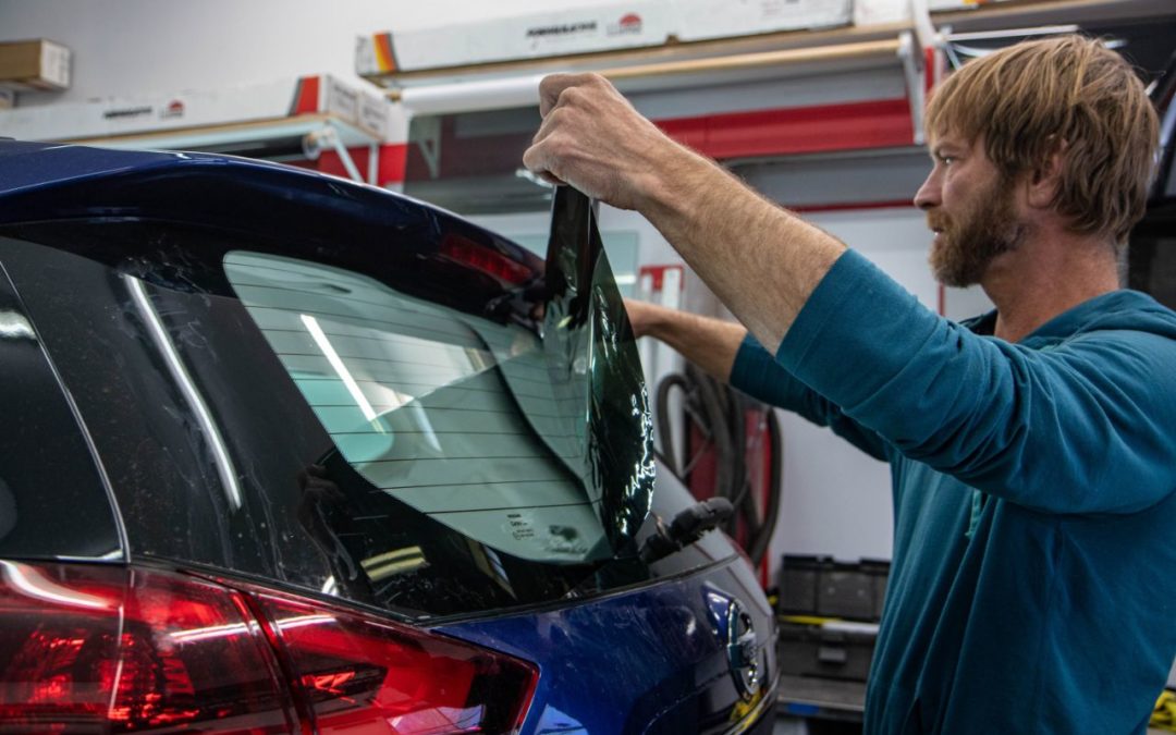 A technician at Inspector's Auto carefully applies window tint to the back window of a vehicle.