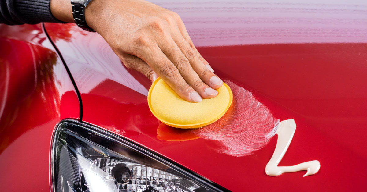 Man applying wax cream to red car's hood