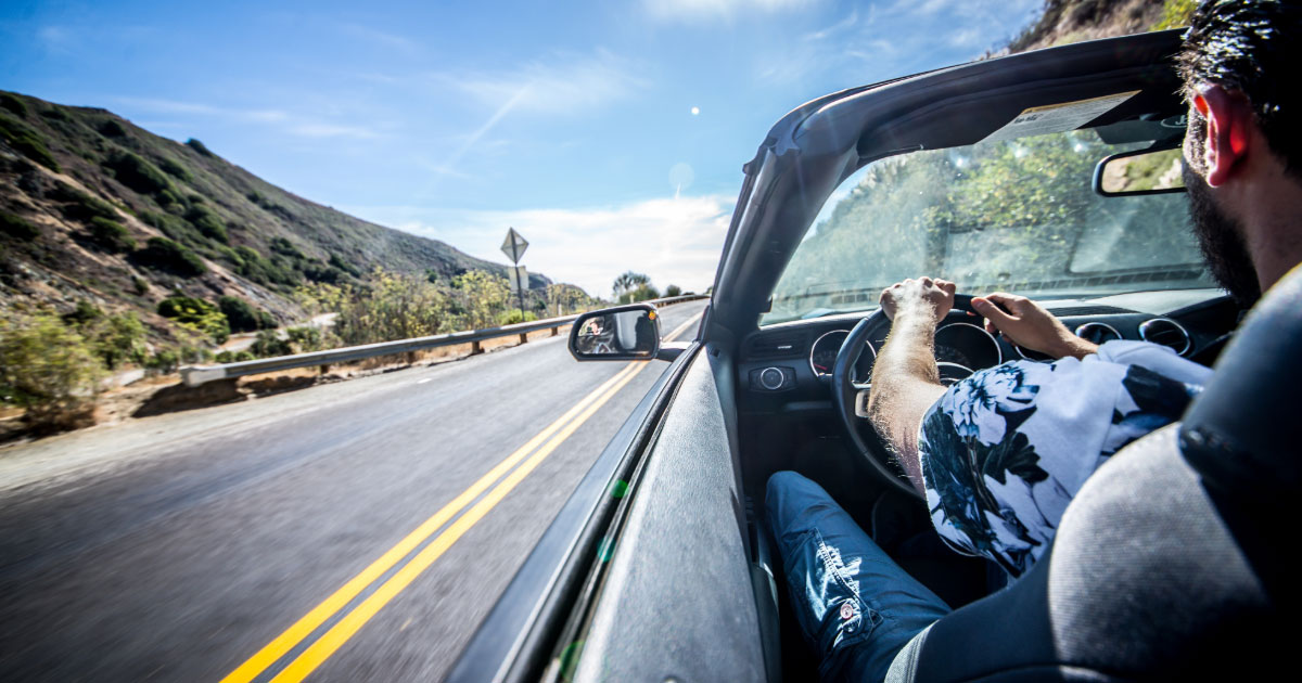 Man driving his convertible along highway with top down