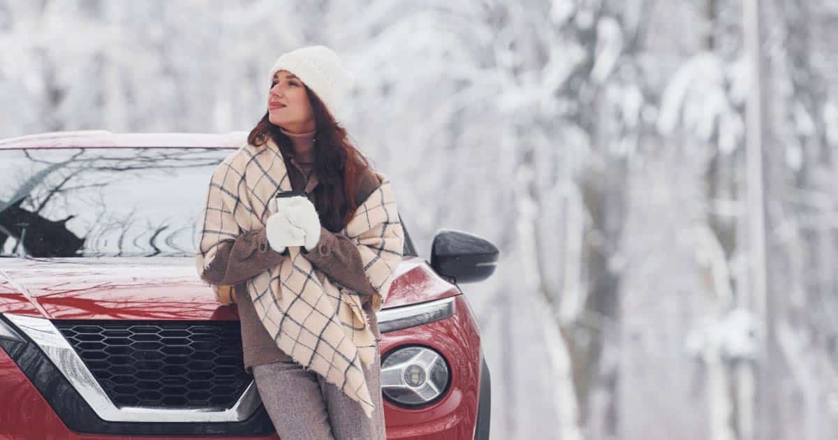 Woman leaning on her car with snow on the ground