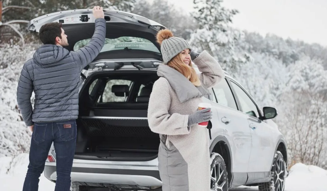 Young couple standing beside SUV with snow on the ground